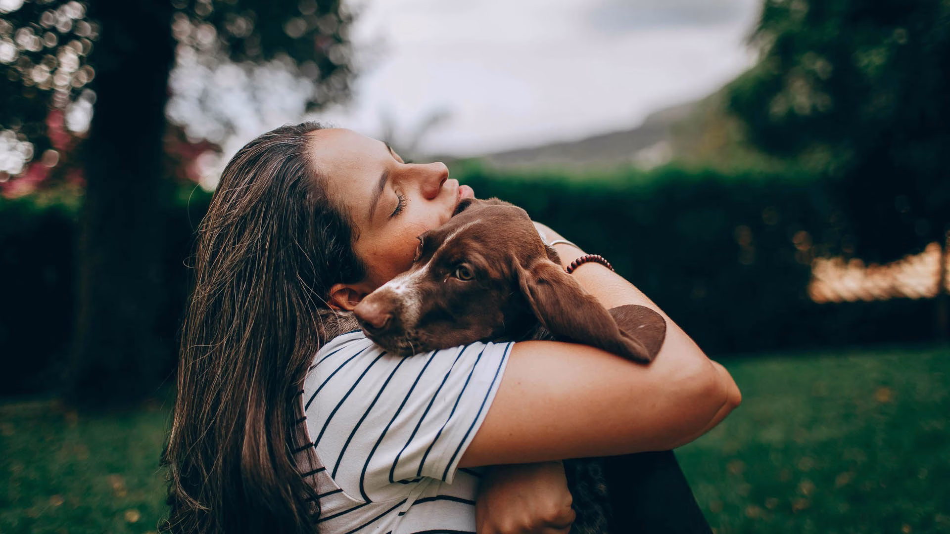 woman in white and black stripe shirt hugging brown short coated dog